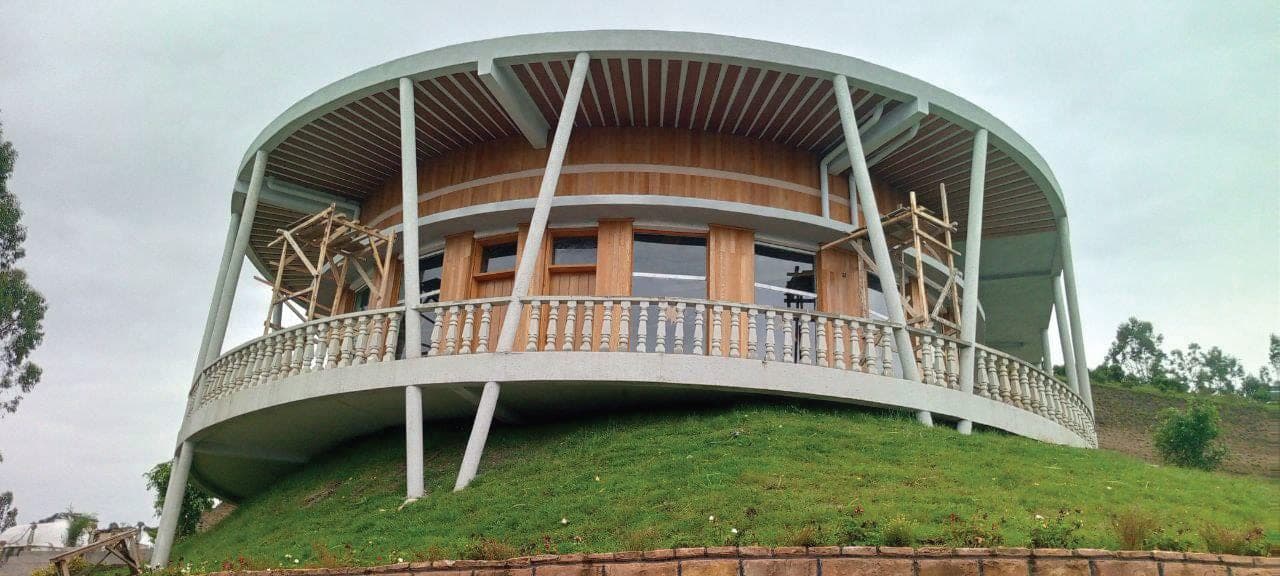 በአረንጓዴ ኮረብታ ላይ የተጠናቀቀ ክብ ቅርጽ ያለው በእንጨት የተለበጠ ሕንፃ